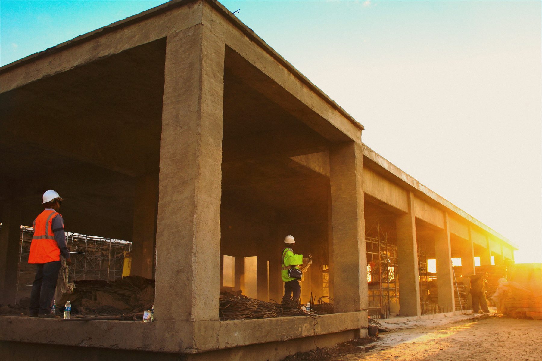 A public building under construction at golden hour with two workers on site.